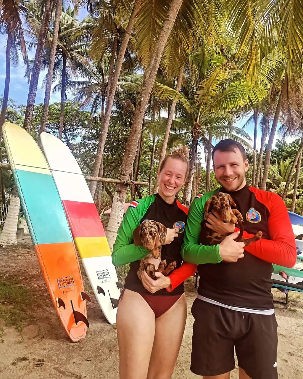 Surf students holding Ron and Morita, the dachshund mascots of Indio Surf School in Playa Sámara